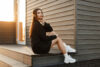 Egy nő chunky sneakerben ül egy fából készült fal közelében