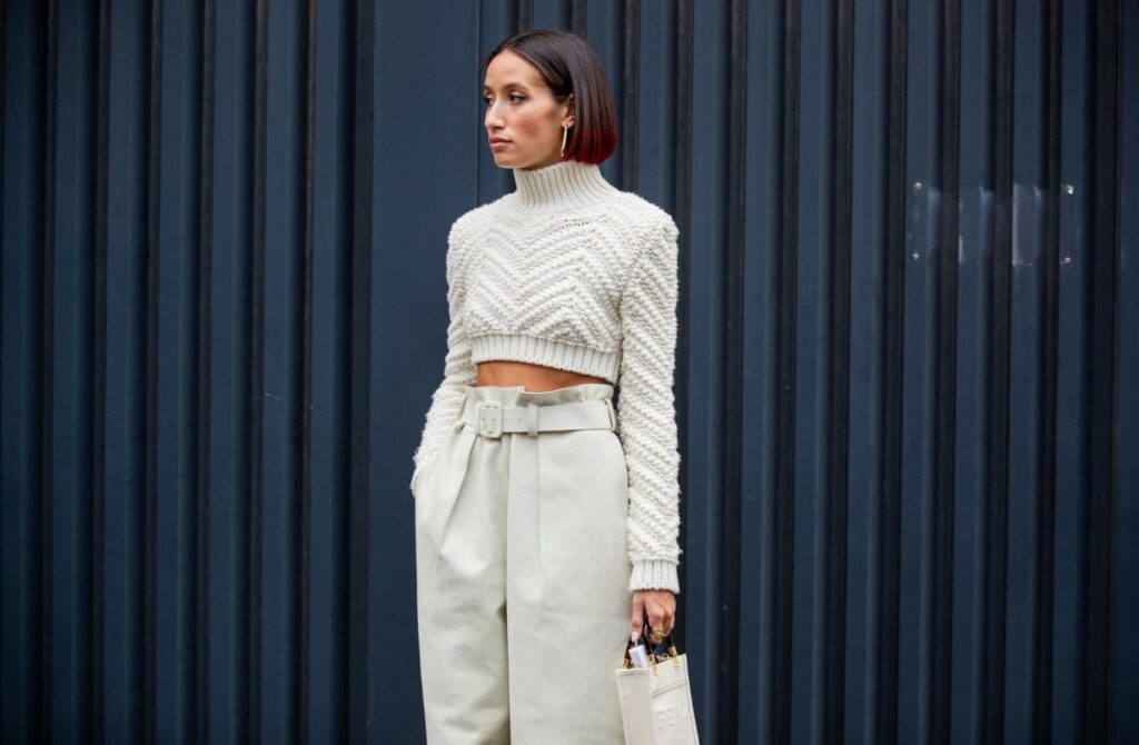 Modell egy rövid, kötött, fehér crop-top pulóverben és magas derekú nadrágban
