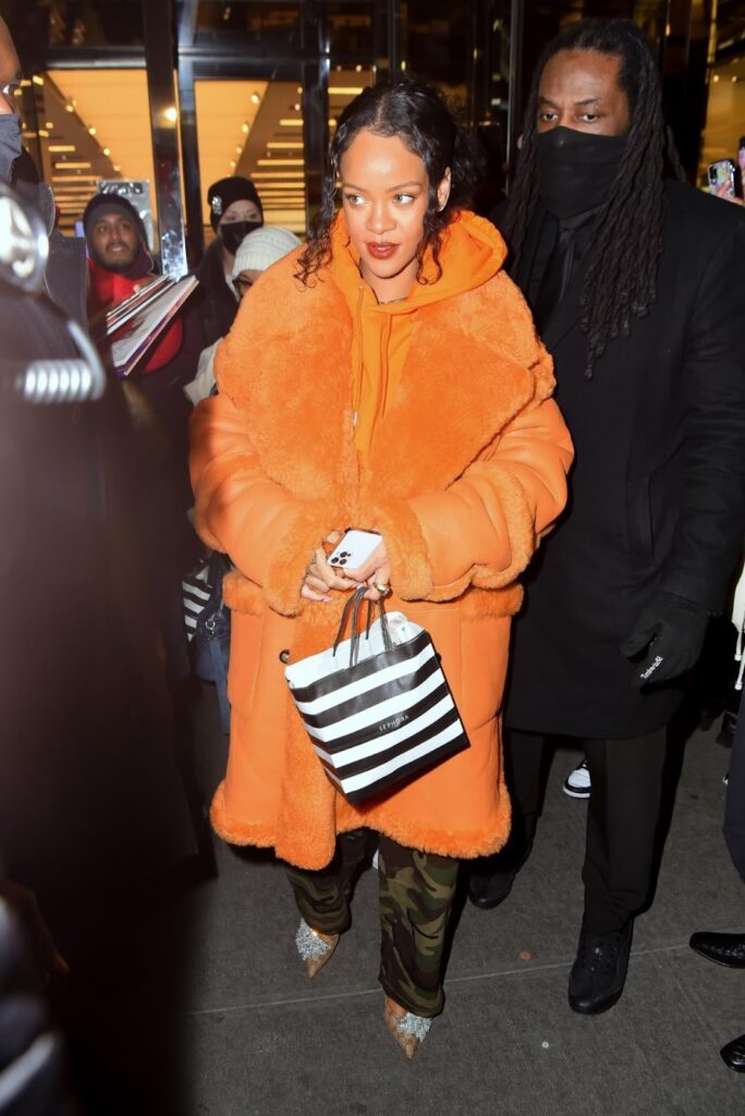 Rihanna katonai stílusú cargo nadrágban, narancssárga kapucnis felsőben, valamint ugyanolyan színű kabátban és magassarkúban