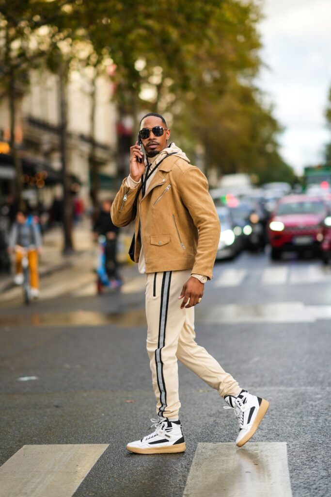 Egy férfi modell oldalcsíkos melegítőnadrágban, barnás dzsekiben és flatform, magasszárú sneakerben