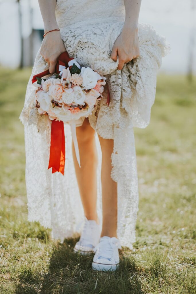 Egy boho stílusú, fehér tornacipőt viselő nő, kezében egy virágcsokor