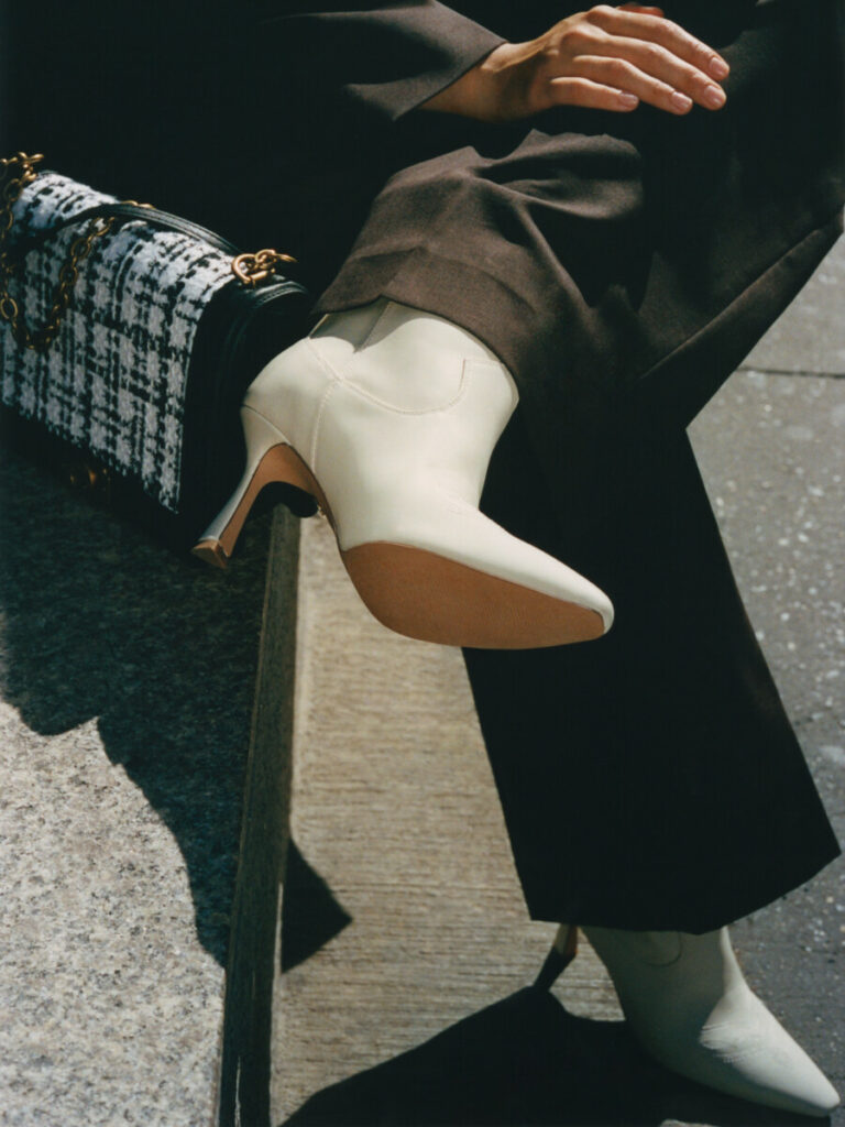 egy nine west márkájú táskát és fehér bokacsizmát viselő nő