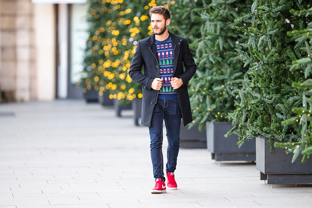 Piros sneakert, elegáns kabátot és csúnya karácsonyi pulóvert viselő férfi